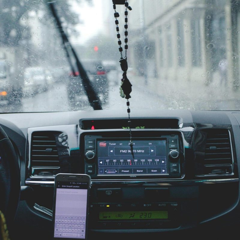 Car interior with driver navigating rainy cityscape using phone and dashboard.