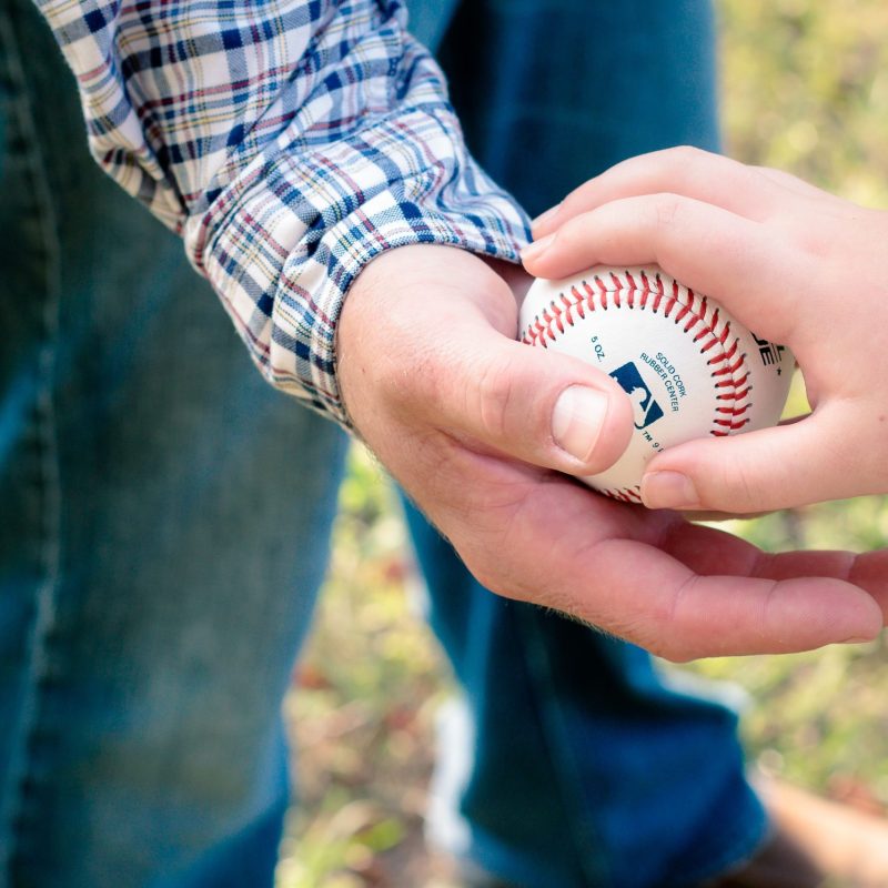 A close-up of a father and son passing a baseball outdoors on a sunny day.